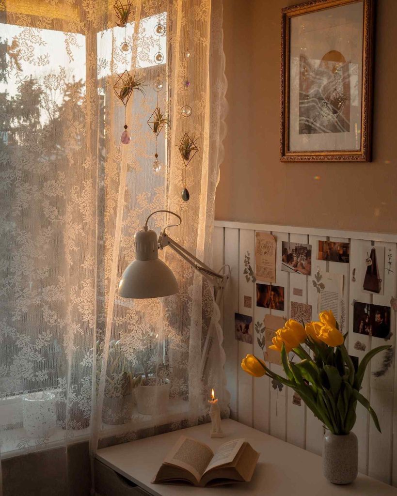 Cozy workspace with lace curtains, tulips, and a glowing candle.