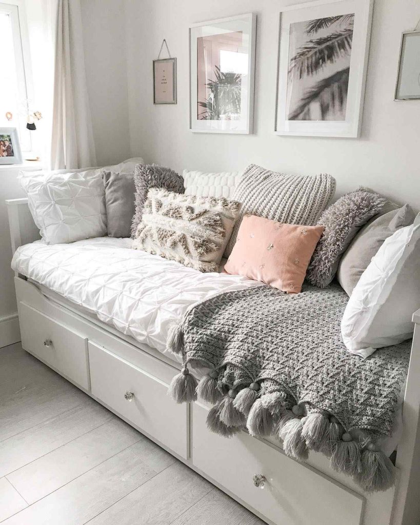 White daybed with neutral pillows and a tassel throw, framed by wall art and natural light.