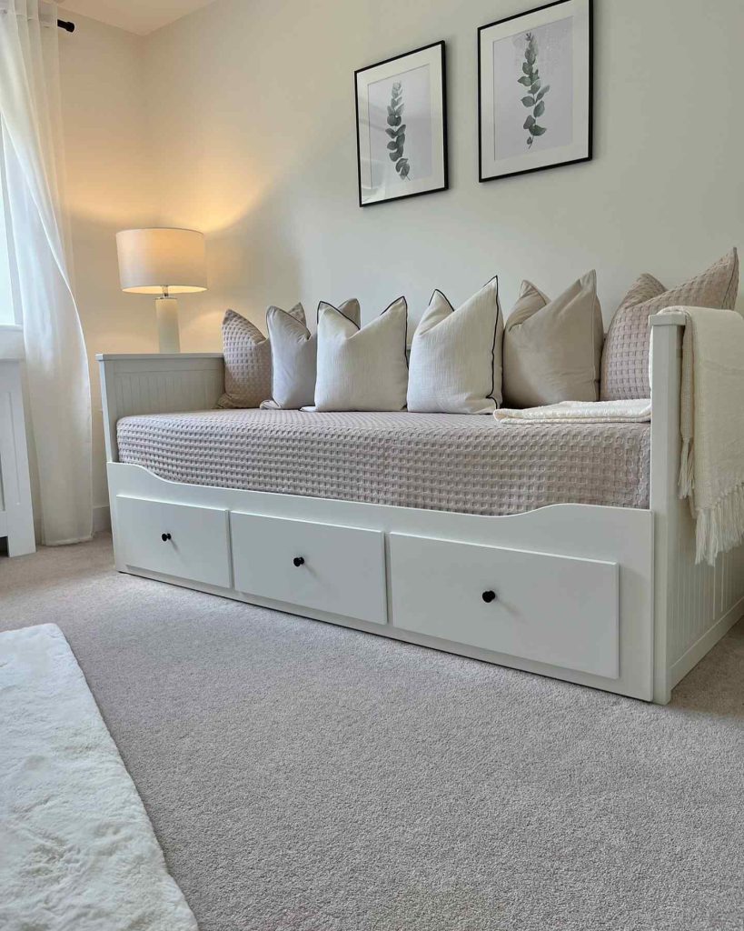 White daybed with neutral pillows, bedside lamps, and framed botanical prints on the wall.