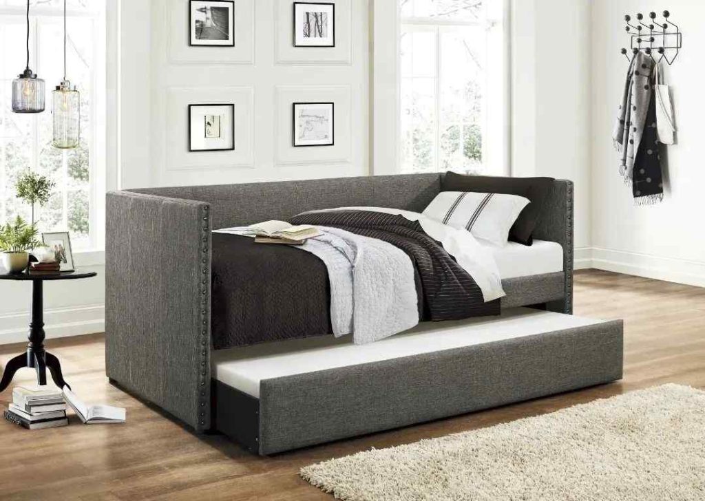 Gray upholstered daybed with a trundle, accented with dark bedding and modern decor.