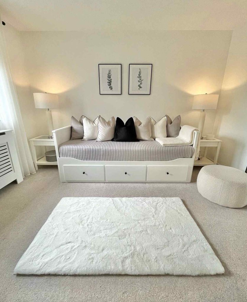 White daybed with a mix of neutral and black pillows, illuminated by warm lighting.