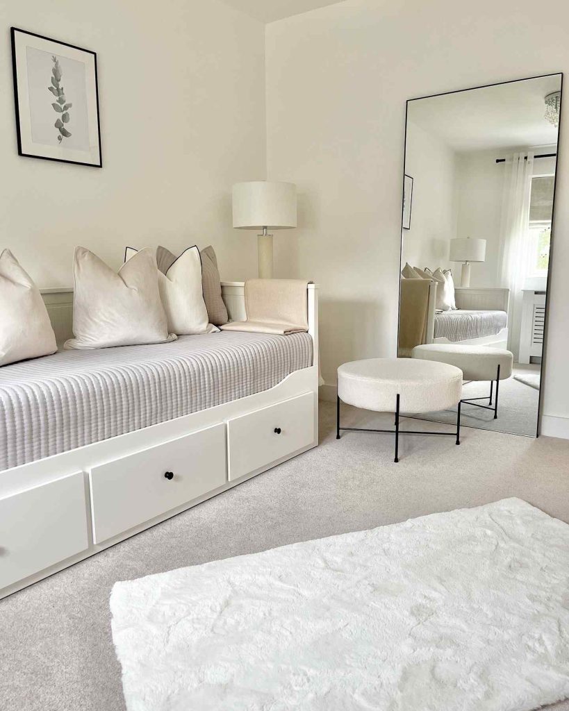 White daybed with soft beige pillows and a large standing mirror in a bright, airy room.