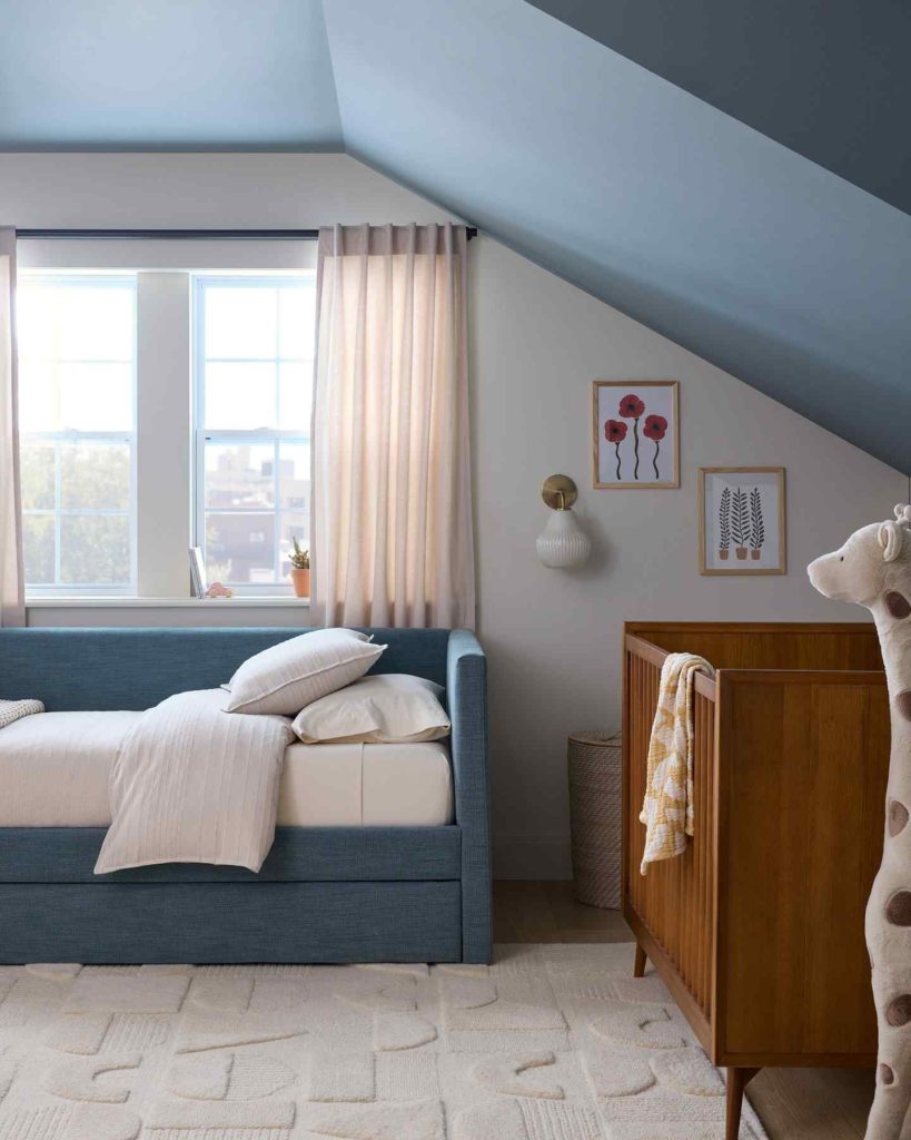 Blue upholstered daybed in a lofted nursery, paired with a crib and playful decor elements.