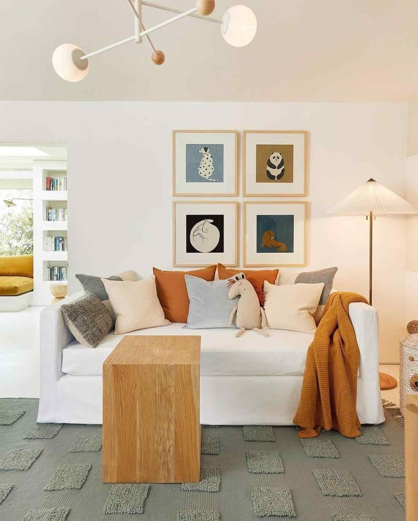  White daybed with warm-toned pillows, colorful wall art, and modern decor in a bright living space.