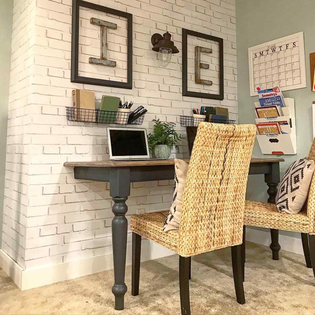 Rustic desk setup with brick wall and woven chairs.