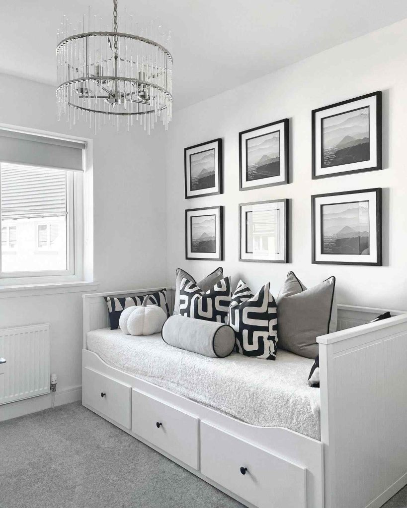 Gray and white daybed with geometric pillows, a chandelier above, and a gallery wall behind.