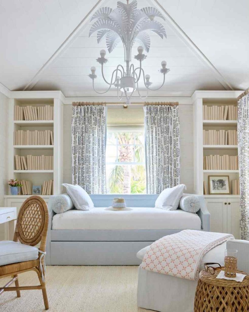 Soft blue daybed in a room with built-in bookshelves, floral curtains, and a palm-leaf chandelier.