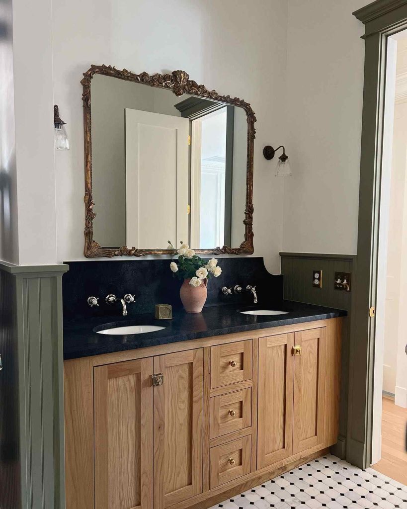 Classic bathroom with light wood vanity and ornate gold mirror.