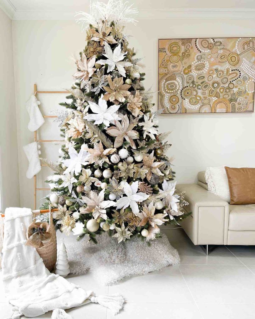 Tree with poinsettias and gold ornaments in a neutral room.
