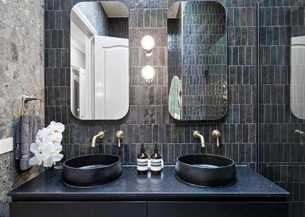 Textured bathroom with black vessel sinks and brass accents.