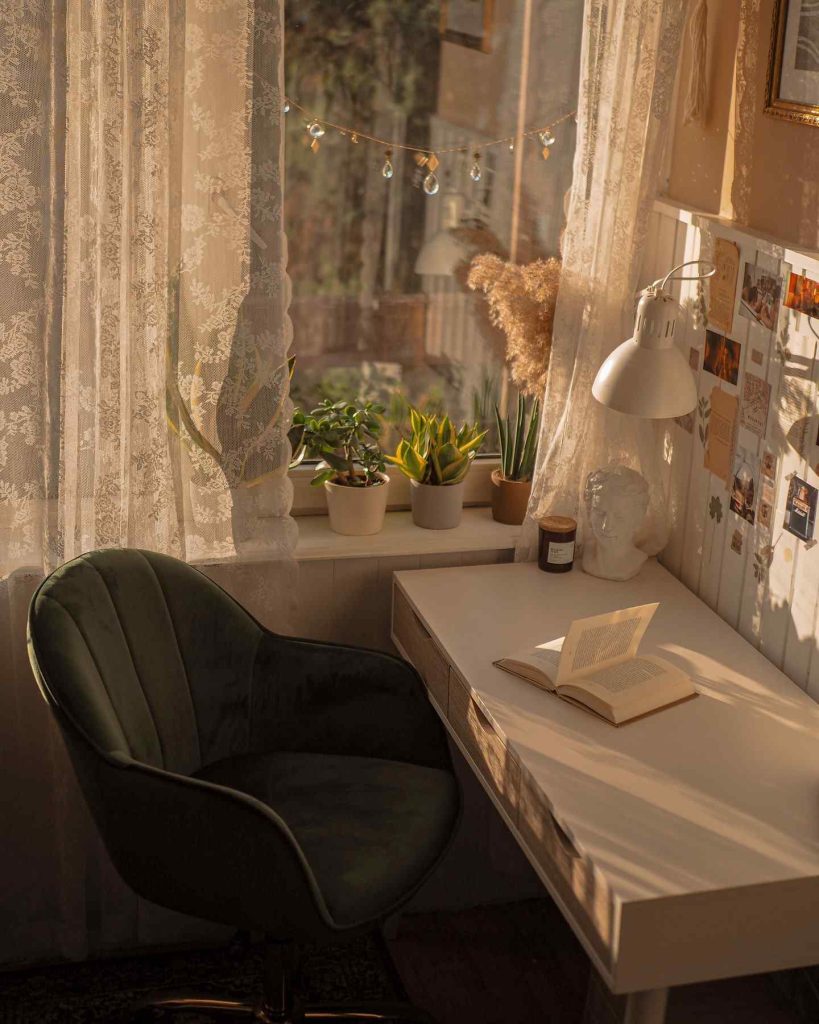 Sunlit desk corner with plants and a velvet chair.