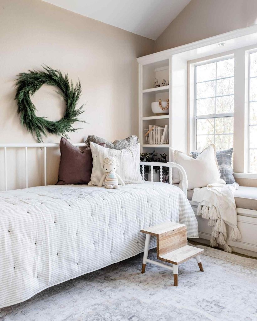 White daybed with textured bedding, festive greenery wreath, and a large window nook.