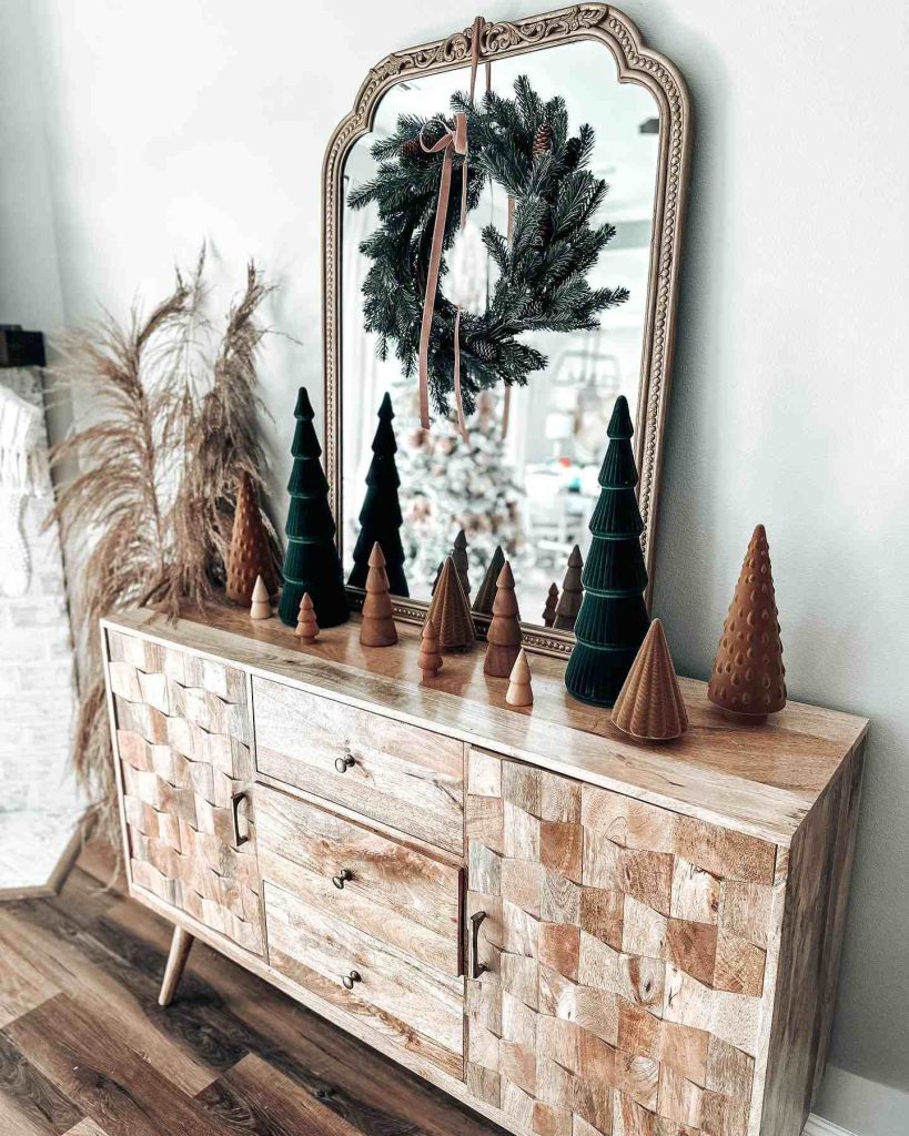 Wooden console with mini trees and a greenery wreath.
