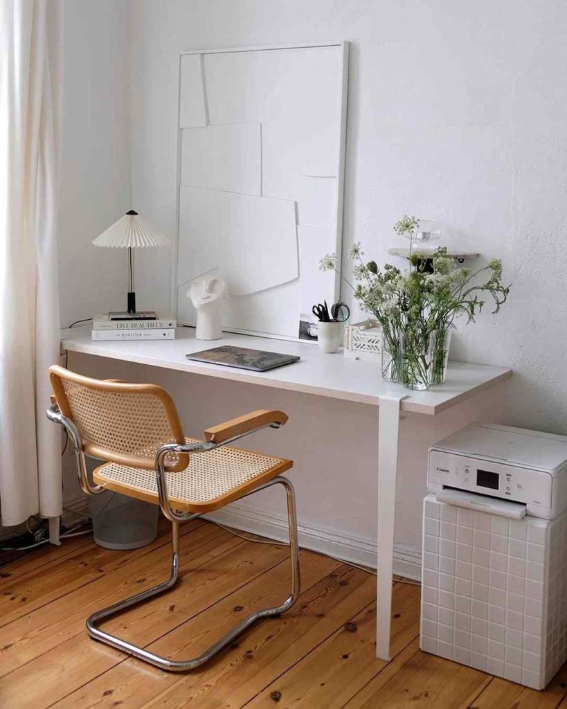 Minimalist white desk with greenery and woven chair.