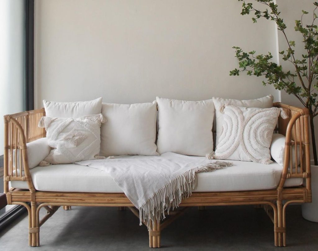 Natural rattan daybed with white cushions, textured pillows, and a potted tree in the corner.