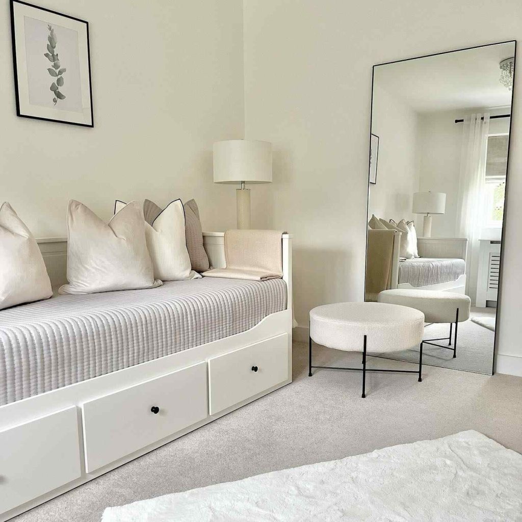 White daybed with beige pillows, a floor mirror, and a soft area rug in a clean, bright room.