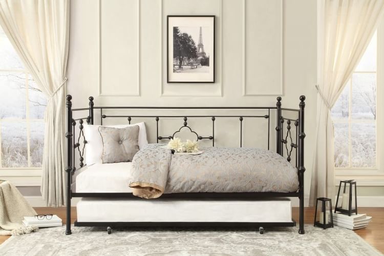 Black wrought iron daybed with a trundle, soft bedding, and sheer curtains in a vintage-inspired room.