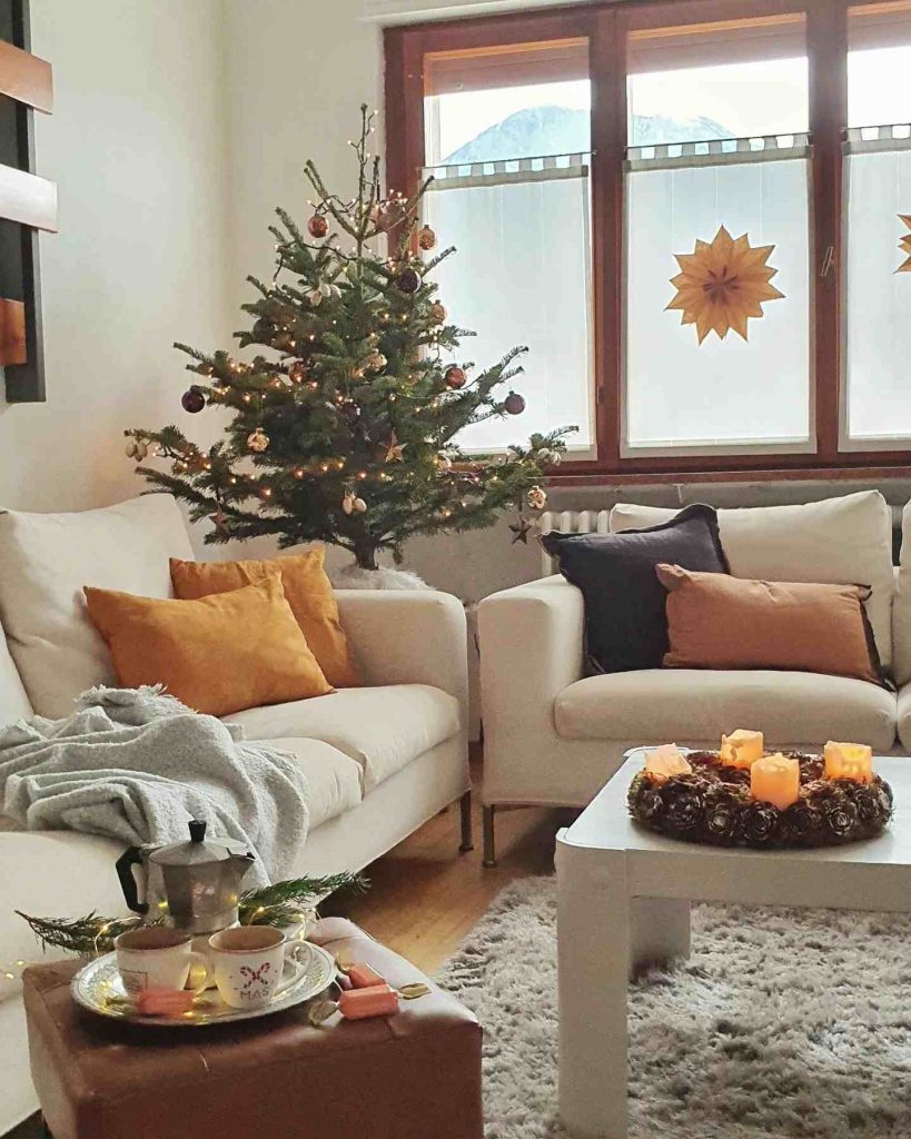 Living room with a small tree, warm throws, and candles.
