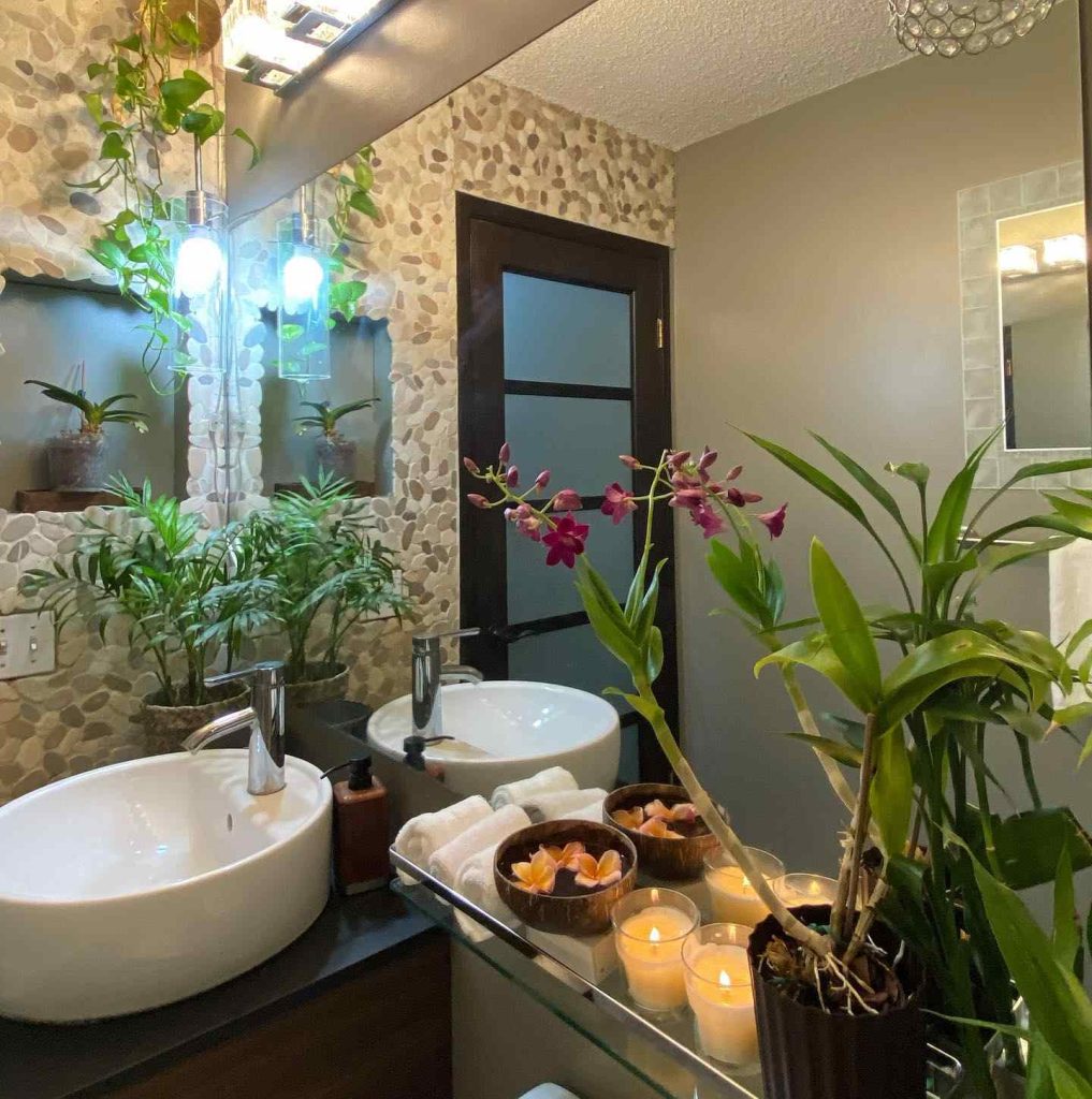 Spa-like bathroom with stone basin, orchids, and a glowing candle arrangement.
