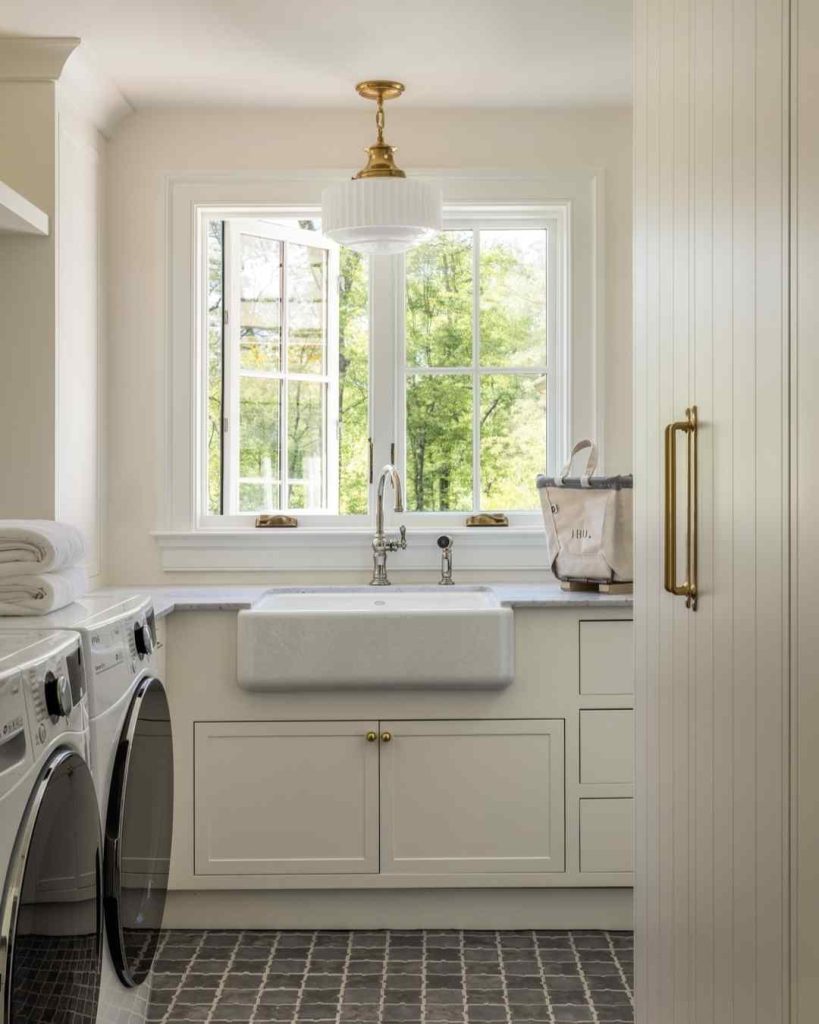 Minimalist white laundry room with black machines and gold fixtures.
