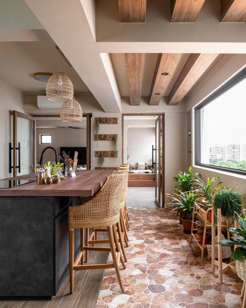 Modern rustic kitchen with stone-look flooring, wood beams, and woven rattan chairs.
