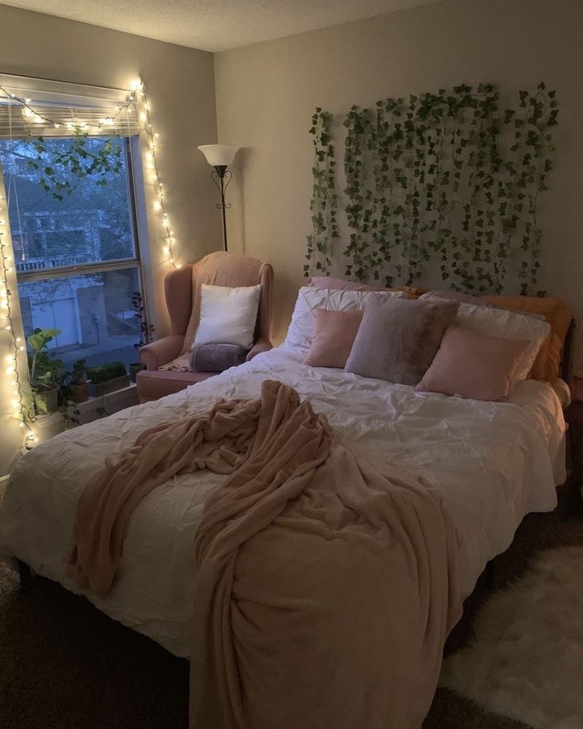 Cozy bedroom with ivy wall decor, blush tones, and warm fairy lights.