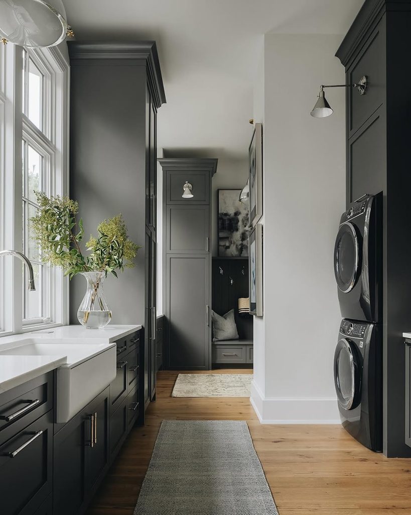 Moody gray laundry room with stacked machines, gold accents, and a pet nook.
