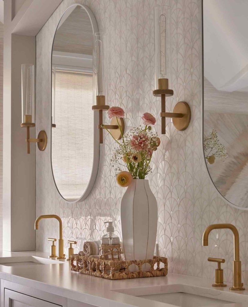 Elegant bathroom with gold faucets, floral wallpaper, and fresh blooms.
