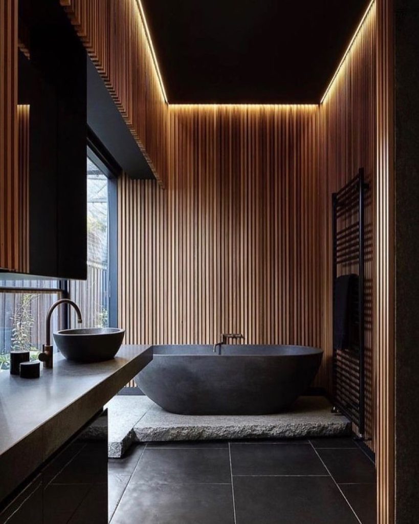 Minimalist bathroom with dark stone tub and vertical wood paneling.
