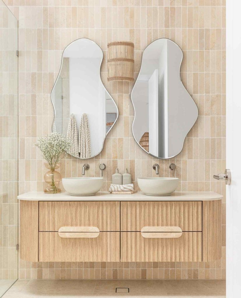 Light wood vanity with artistic mirrors and soft beige tiles.
