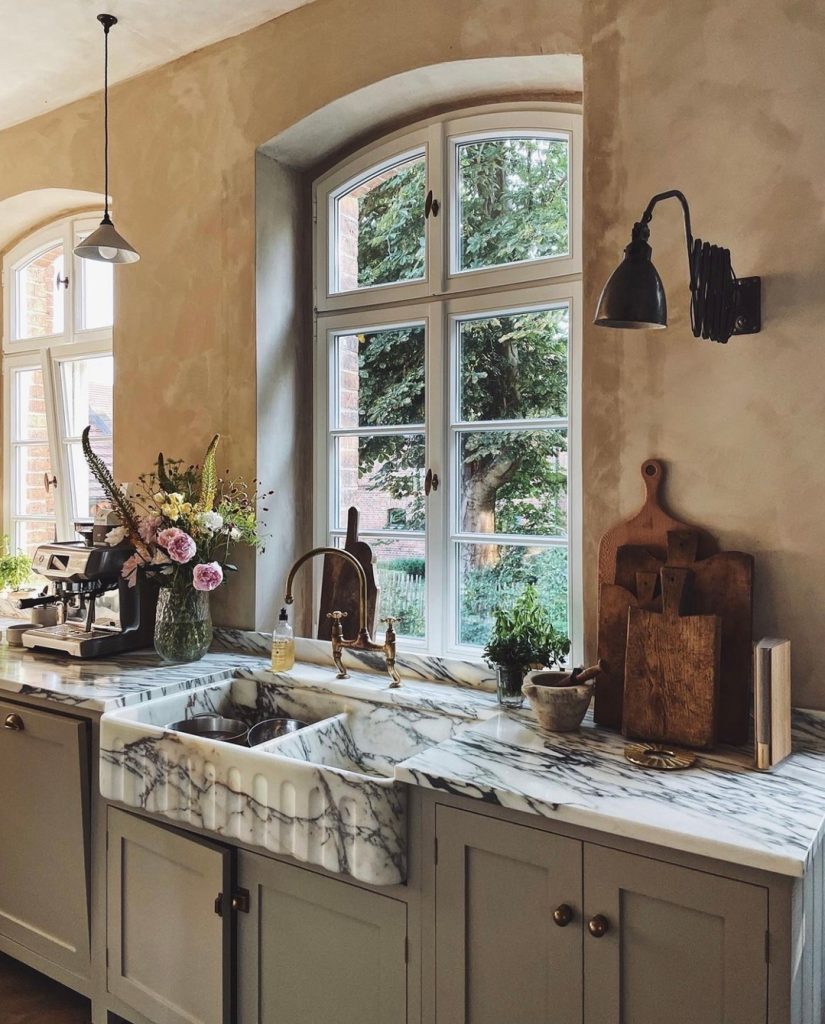 Elegant kitchen with veined marble sink, muted cabinets, and arched windows.
