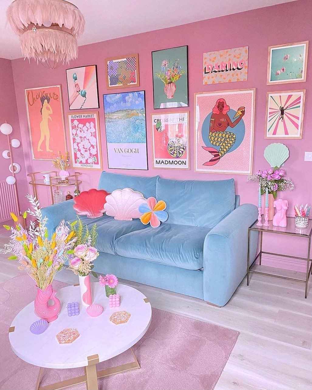 Pink-themed room with pastel furniture, shell pillows, and artistic gallery wall.
