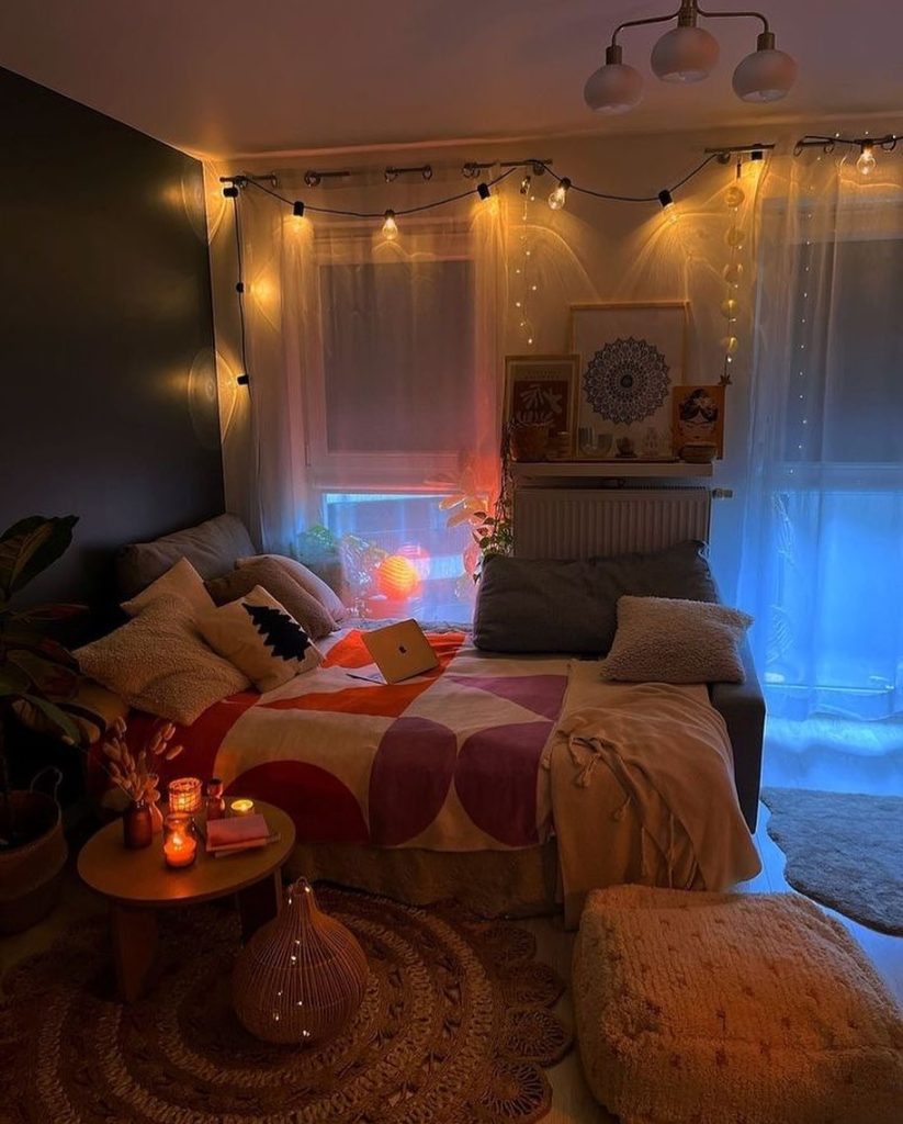 Cozy bedroom with string lights, candles, and layered colorful textiles.