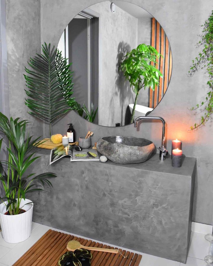 Modern bathroom with concrete walls, stone basin, and soft candlelight.
