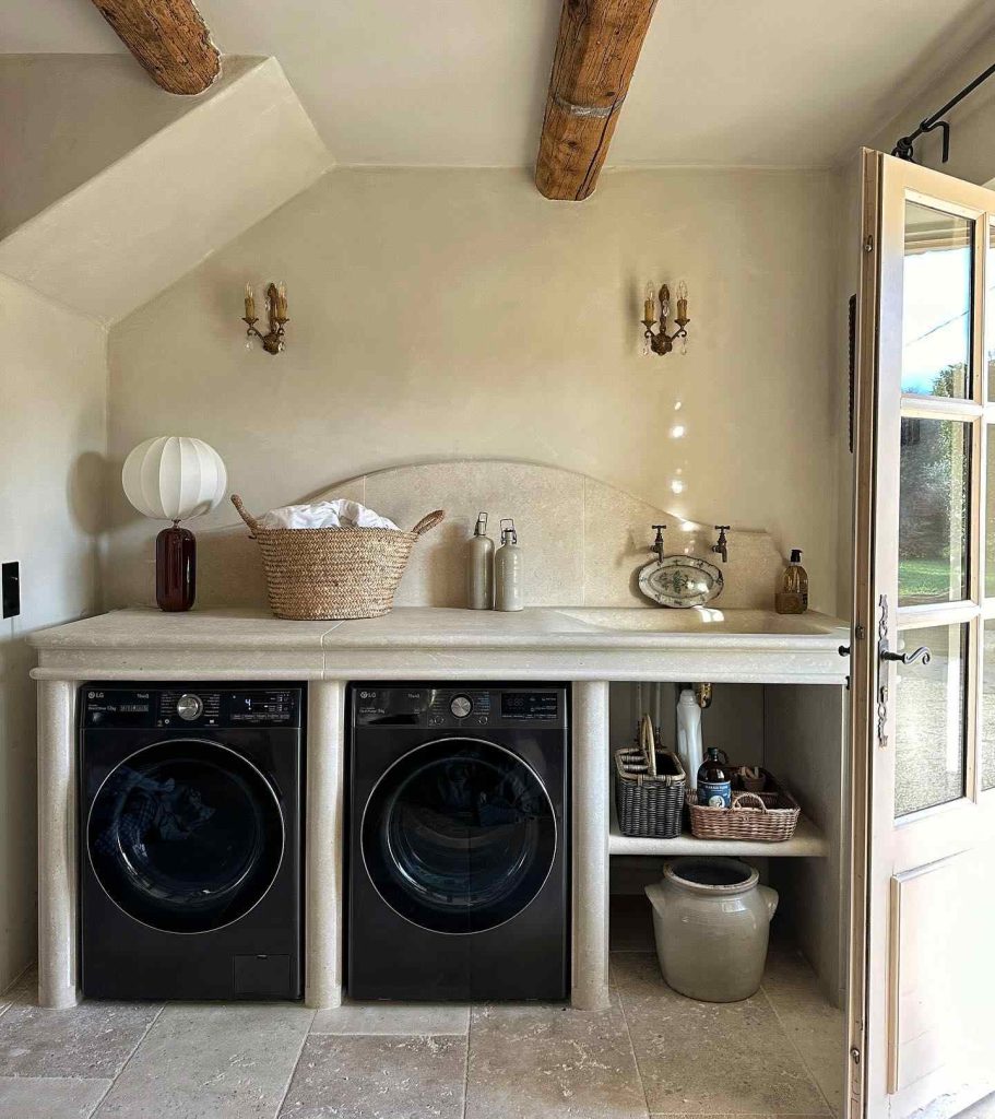 European-style laundry room with stone counters, rustic beams, and black machines.
