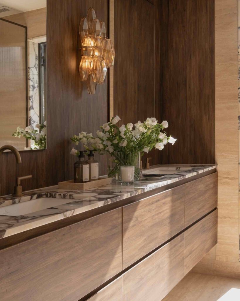 Bathroom with dark wood, marble countertop, and amber sconces.
