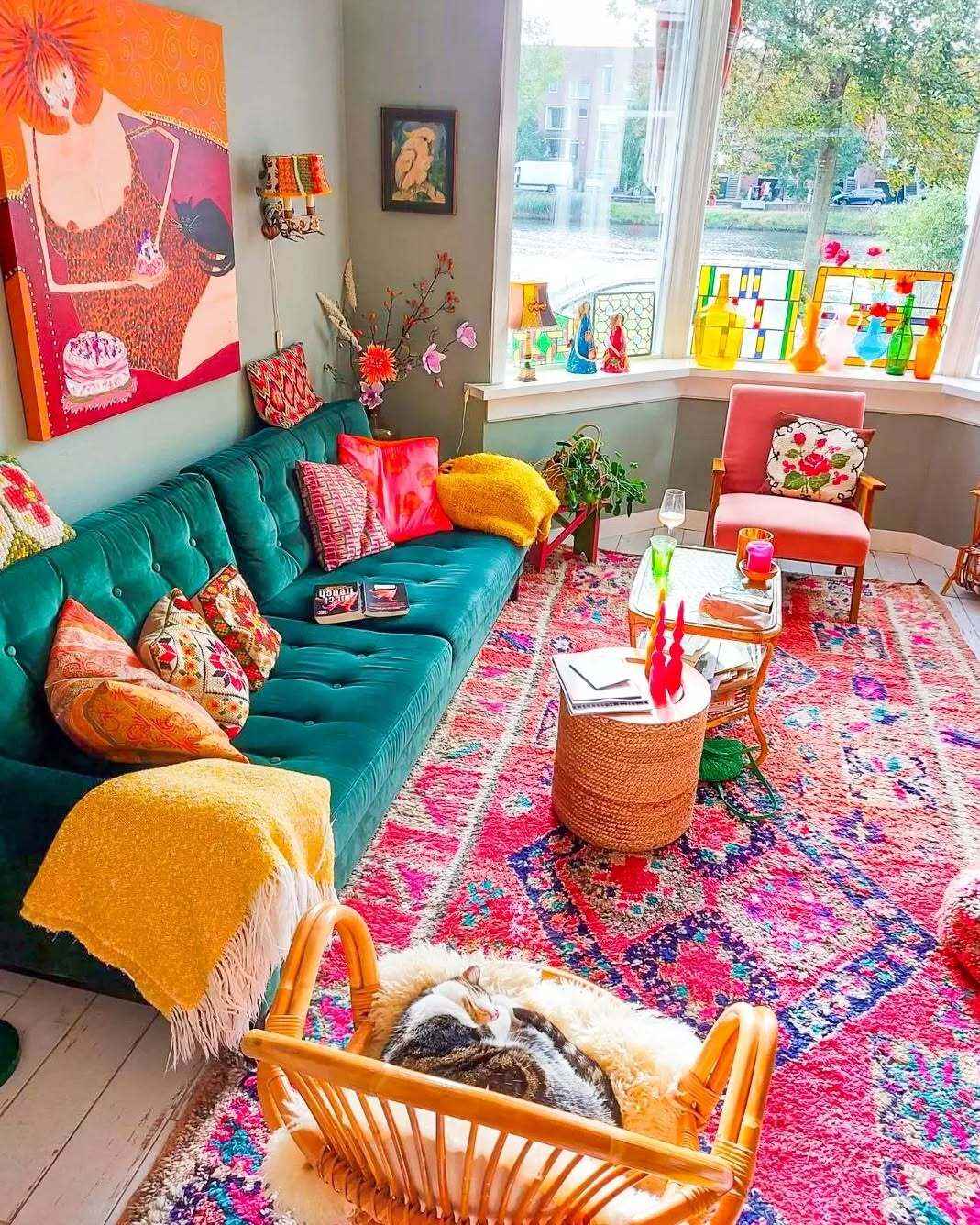 Bohemian living room with green velvet sofa, pink rug, and cozy cat in a chair.
