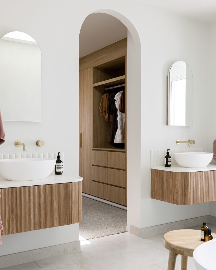 Arched doorway bathroom with floating vanities and brass fixtures.
