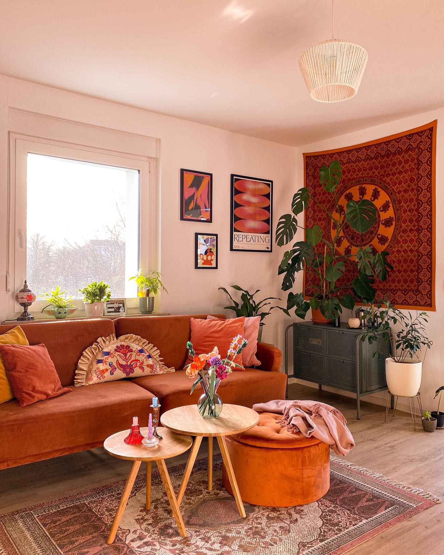 Earthy living room with rust sofa, layered textures, and boho tapestry wall.
