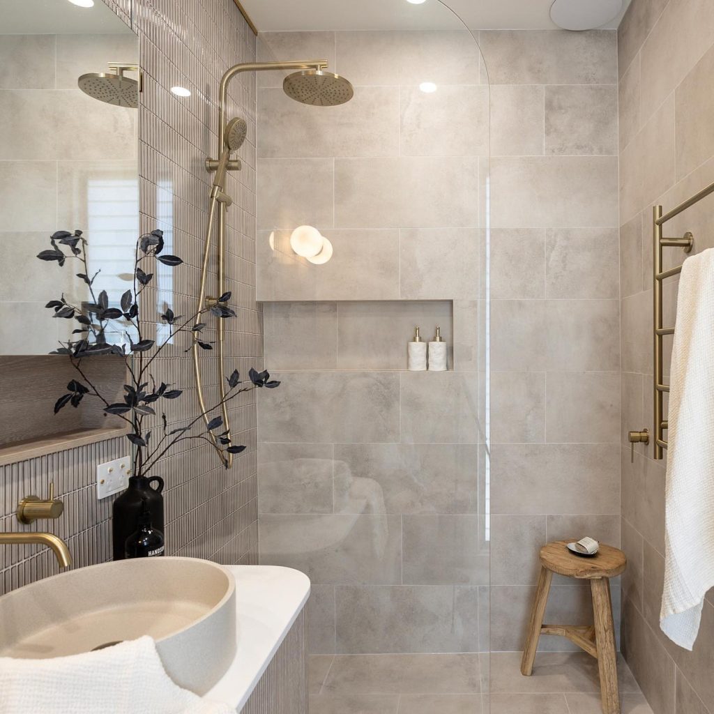 Neutral bathroom with brass accents and a rustic wooden stool.
