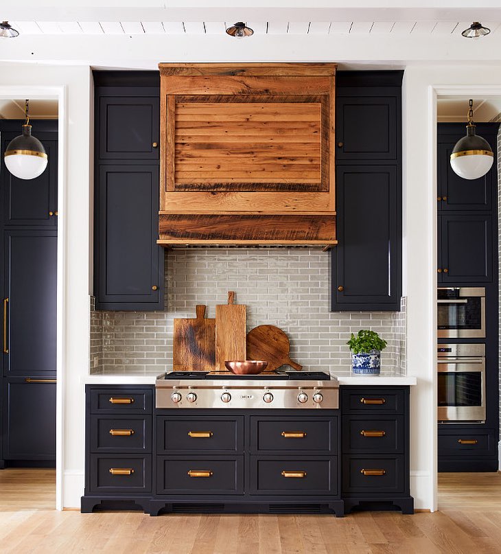 Bold navy kitchen cabinets with brass hardware and a statement wooden hood.
