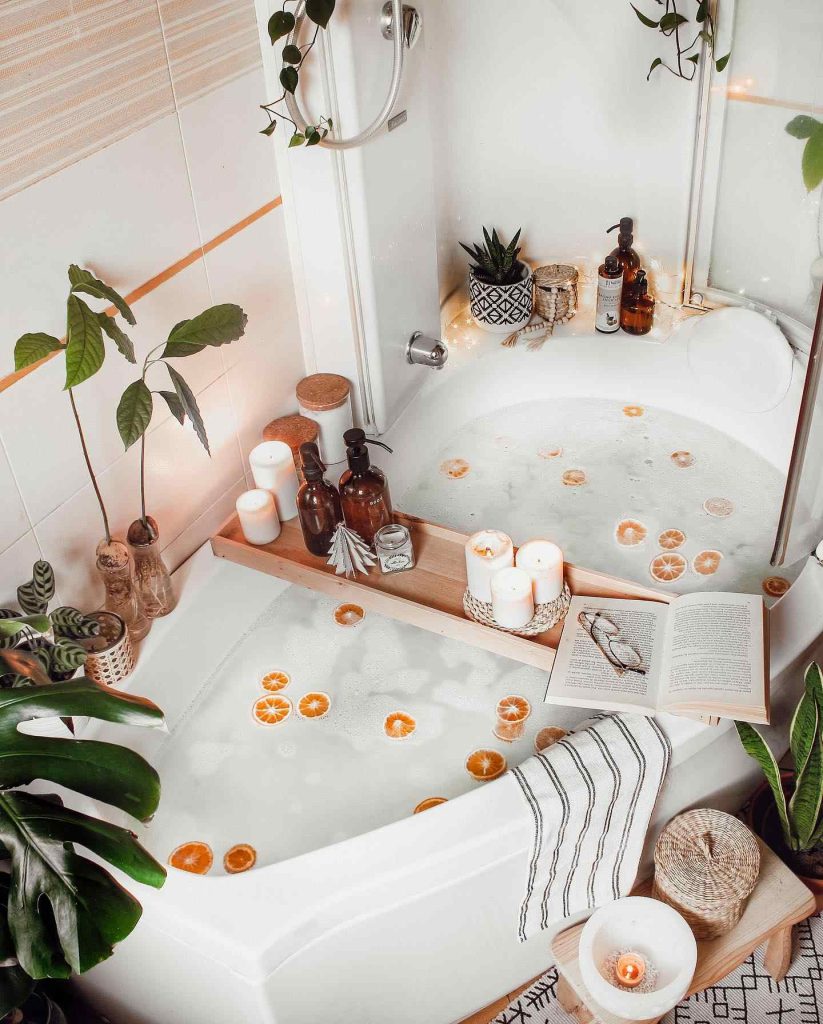 Relaxing bathtub surrounded by candles, citrus slices in the water, and lush greenery.
