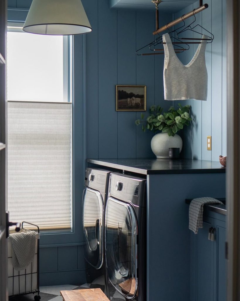 Moody blue laundry room with a hanging rod and modern black appliances.
