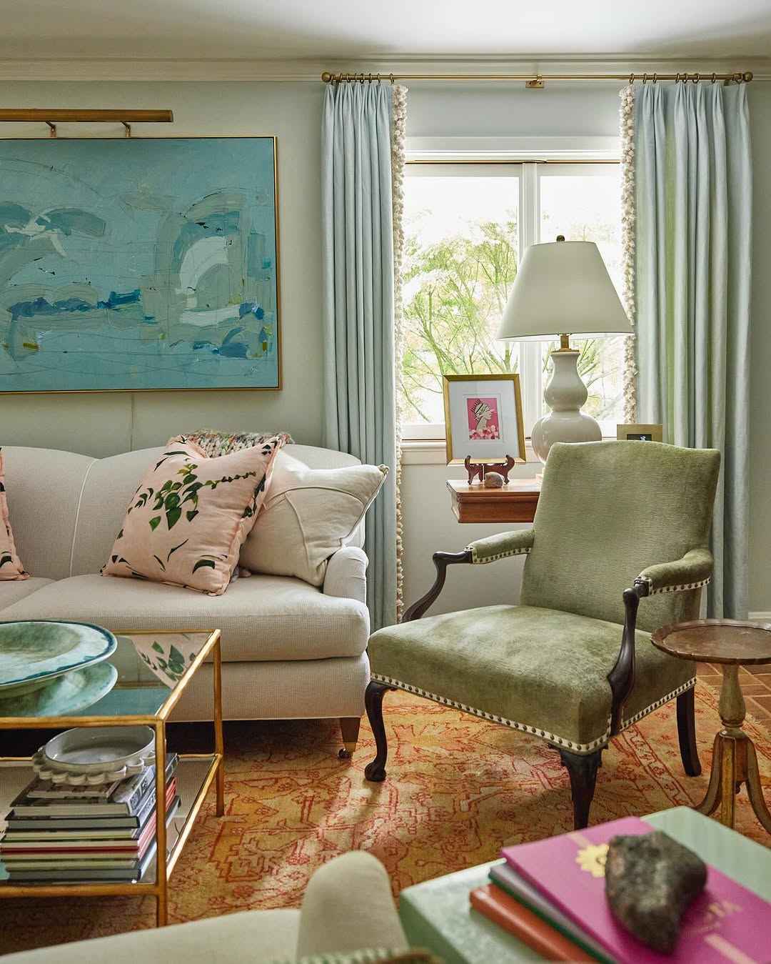 Traditional living room with soft blue curtains, abstract artwork, and velvet chair.
