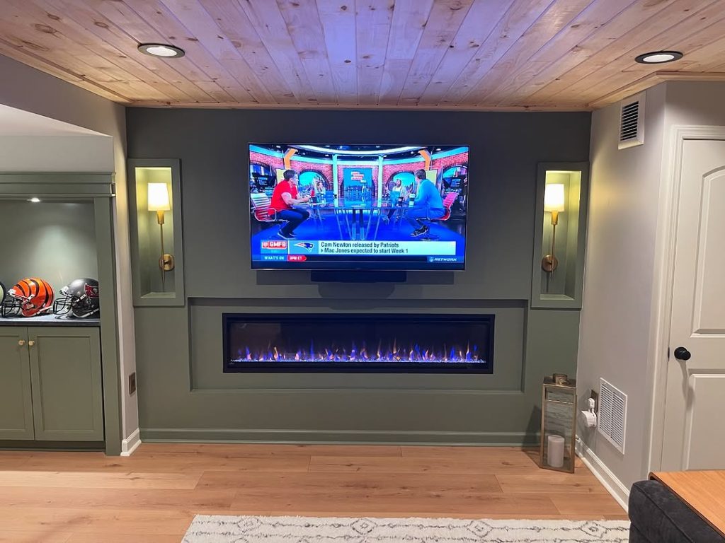 Basement TV area with green walls, built-in sconces, and an electric fireplace.
