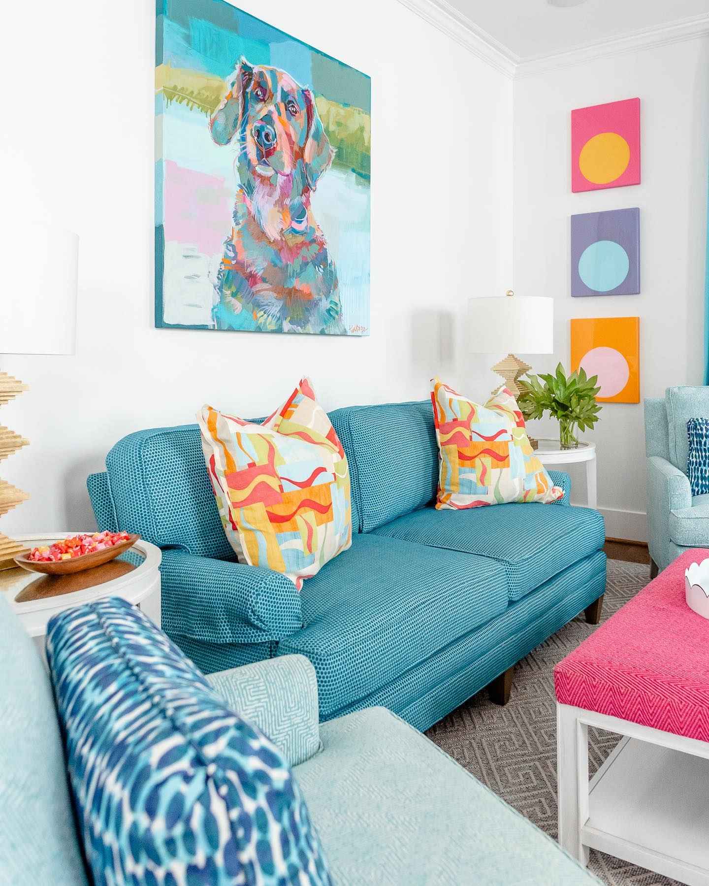 Bright living room with teal furniture, colorful pillows, and dog portrait art.
