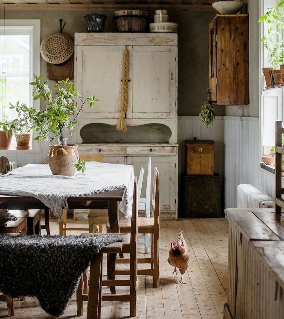 Charming countryside kitchen with a vintage hutch, wooden table, and a free-roaming chicken.
