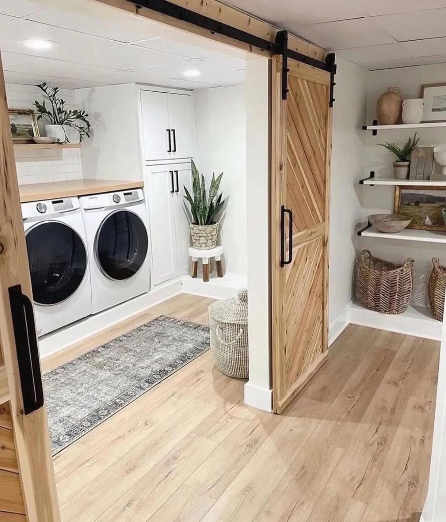 Farmhouse-style laundry room with barn doors, open shelves, and potted plants.
