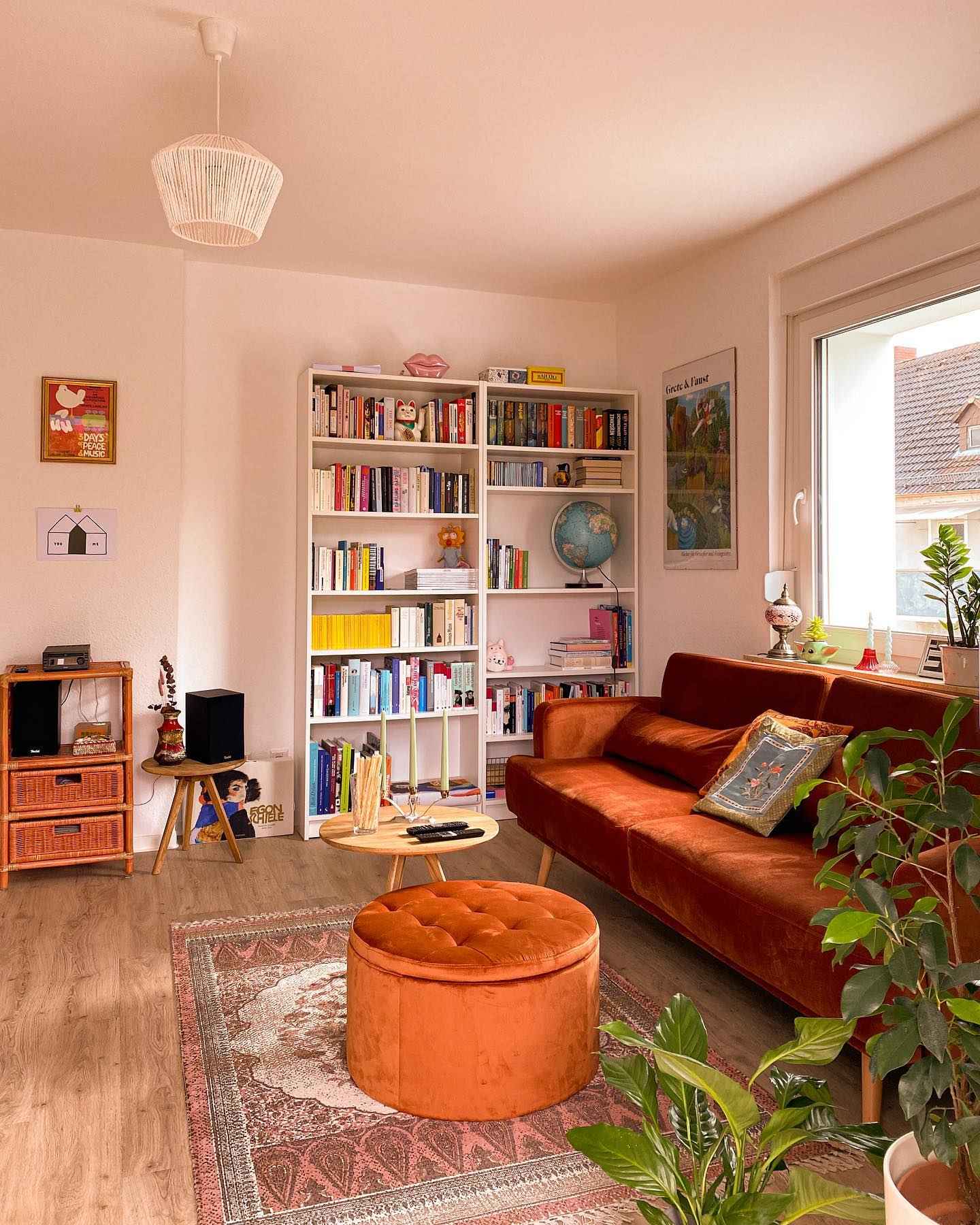 Warm-toned living room with rust sofa, bookshelves, and a cozy ottoman.
