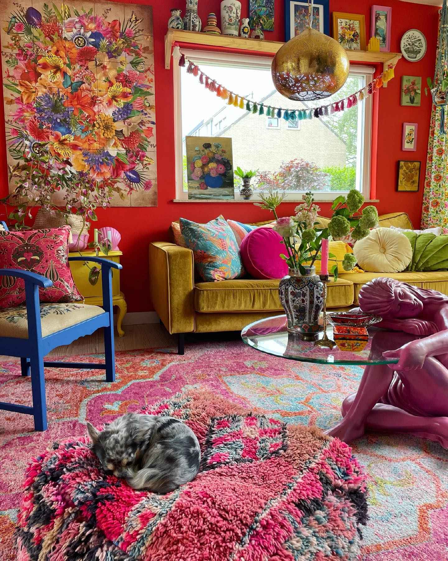 Eclectic red living room with floral wall art, colorful accents, and a pink statue table.
